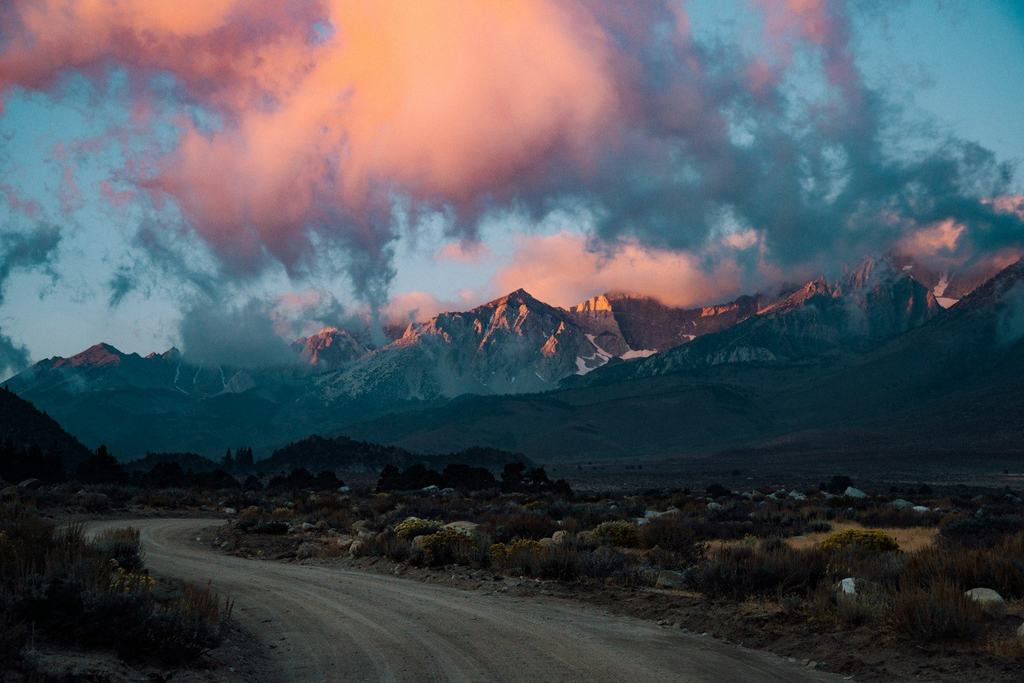 A dirt road through the desert toward mountains under a pink sky