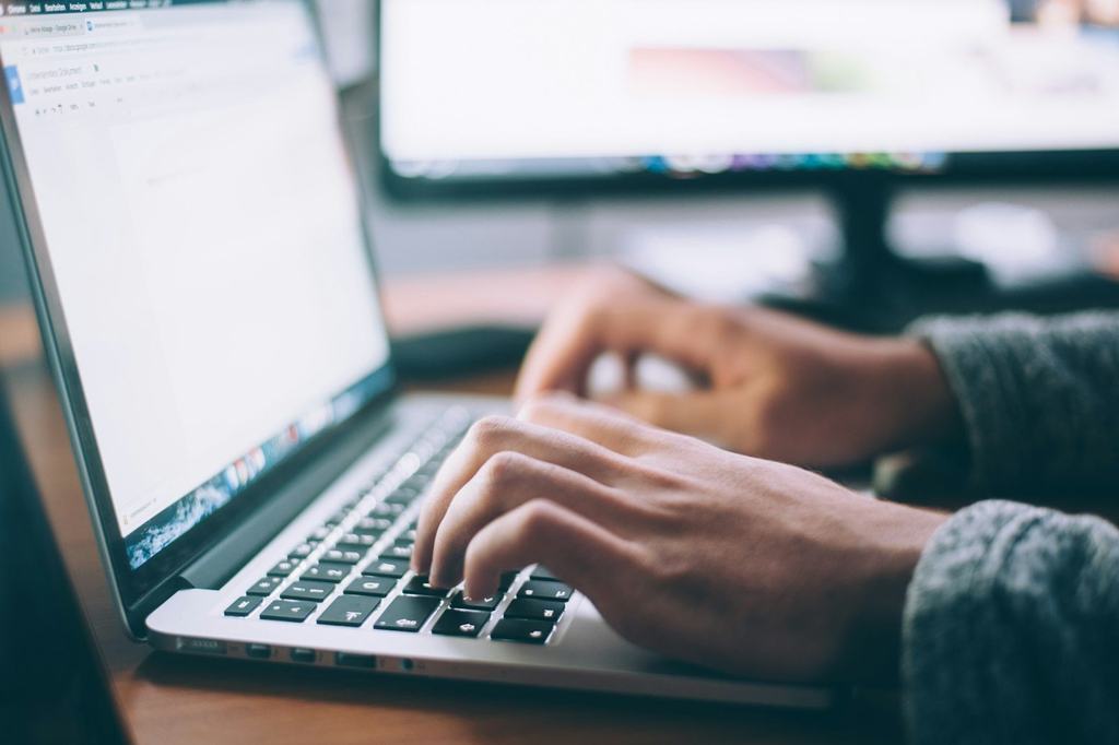 Hands typing on a laptop at a wooden desk
