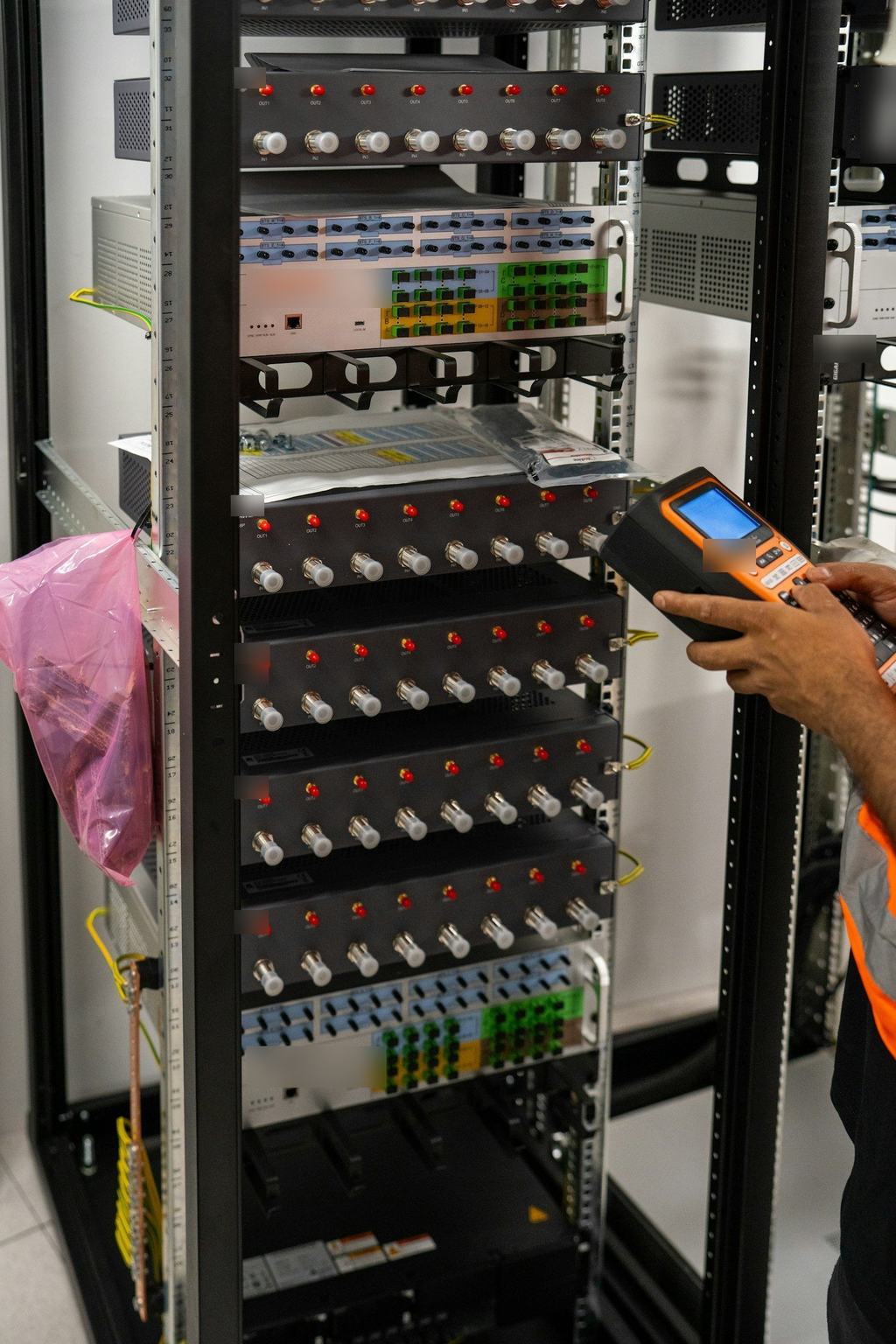 A technician's hands using a handheld tester at a network rack